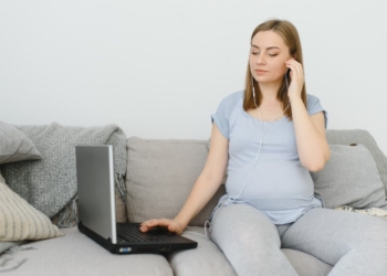 Attractive pregnant woman touching tummy and using laptop on bed